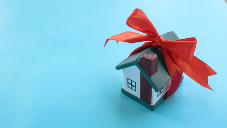 Miniature House with Red Ribbon Bow on Light Blue Background - Real Estate Gift Conceptの写真素材
