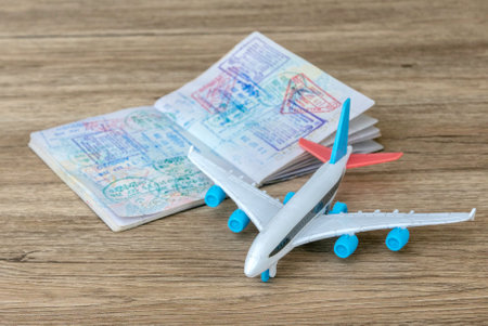 Title: Travel Essentials: Passport with Stamps and Toy Airplane on Wooden Surfaceの写真素材