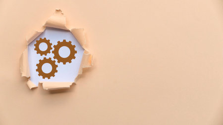 Torn Paper Revealing Three Brown Gears on White Backgroundの写真素材