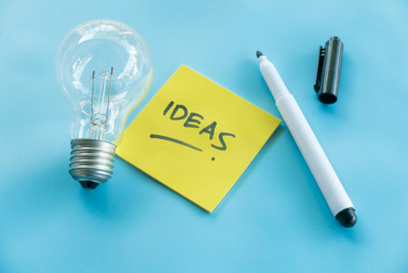 Creative Ideas Concept with Light Bulb, Sticky Note, and Pen on Blue Backgroundの写真素材