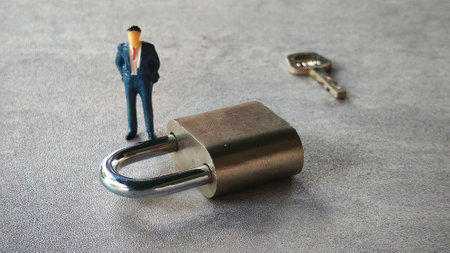 miniature businessman standing beside metallic padlock