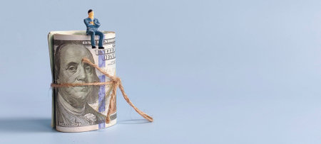 Miniature Businessman Sitting on Rolled US Dollar Bills Tied with Twine.の写真素材
