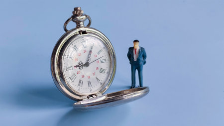 Miniature Businessman Standing Beside an Open Pocket Watch on a Blue Backgroundの写真素材