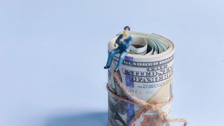 Miniature Businessman Sitting on Rolled US Dollar Bills Tied with Twine.の写真素材
