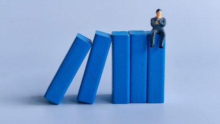 Miniature Businessman Sitting on Blue Blocks with Domino Effectの写真素材