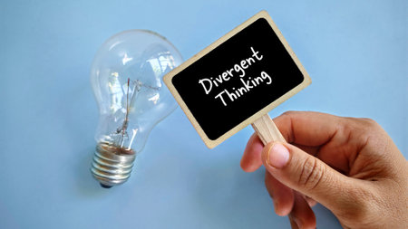 a hand holding notification board written with 'Divergent thinking' with light bulb beside it.の写真素材