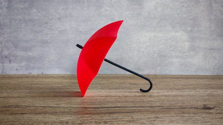 Red Umbrella on Wooden Table, Symbolizing Protection, Insurance, and Risk Management Conceptsの写真素材