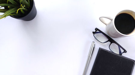 Minimalist flat lay workspace featuring plant, eyeglasses, pen, notebook and a cup of coffee on...