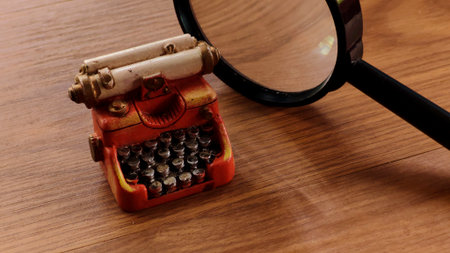 Miniature vintage typewriter with magnifying glass on wooden desk.の写真素材