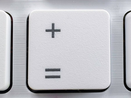 Close-up of a White Plus and Equals Key on a Modern Silver Keyboardの写真素材