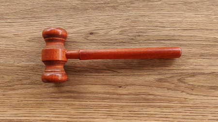 A wooden gavel resting on a textured wood surface, symbolizing law, justice, and authority.の写真素材