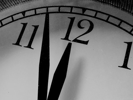 Dramatic black and white close-up of a clock face with hands approaching midnight or noon.の写真素材