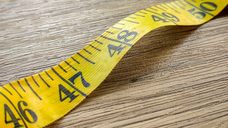 A bright yellow measuring tape lying on a wooden surface, showing inches and measurement markings.