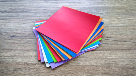 Top-down view of a stack of multicolored origami paper on a wooden background.