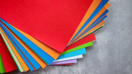 Top-down view of a stack of multicolored origami paper on a gray stone or concrete background.