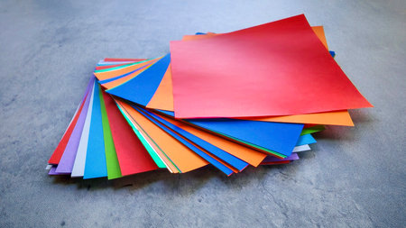 Top-down view of a stack of multicolored origami paper on a gray stone or concrete background.の写真素材