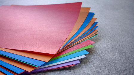 Top-down view of a stack of multicolored origami paper on a gray stone or concrete background.の写真素材