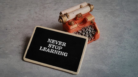 "Never Stop Learning" Motivational Quote on Black Chalkboard with Vintage Miniature Typewriterの写真素材