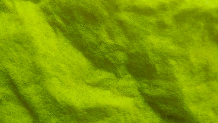 Wrinkled and Textured Green Non-Woven Fabric Close-Up with Soft Fuzz Fibers and Shadow Foldsの写真素材