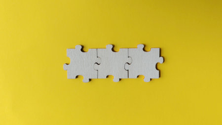 Three interconnected wooden jigsaw puzzle pieces forming a line on a vibrant yellow background,...