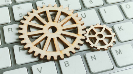 Two wooden cogwheels resting on a computer keyboard, symbolizing digital mechanics, business technology, system processes, and online engineering.の写真素材