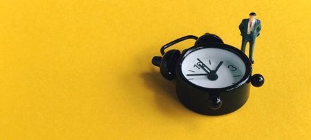 Miniature businessman standing by an alarm clock, symbolizing the urgency of time management,...