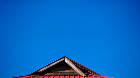 Minimalist Architecture: Sharp Red Roof Peak Against Expansive Deep Blue Sky Background with Ample...