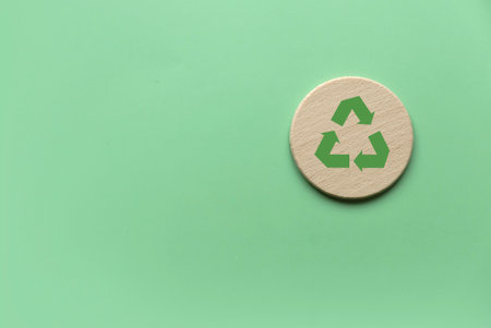 Sustainable Lifestyle Concept: Wooden Coaster with Green Recycle Symbol on Pastel Background Representing Eco-Friendly Living and Environmental Responsibilityの写真素材
