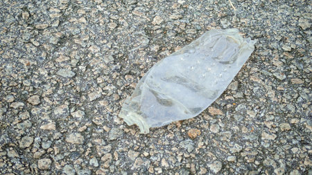 Crumpled Plastic Water Bottle Lying on Rough Pavement: Concept of Environmental Pollution, Waste, and Urban Litterの写真素材