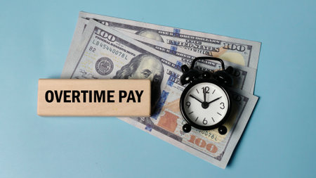 Concept of Overtime Pay with US dollar bills, a wooden block reading OVERTIME PAY, and an alarm clock, symbolizing extra work compensation and time equals money.の写真素材