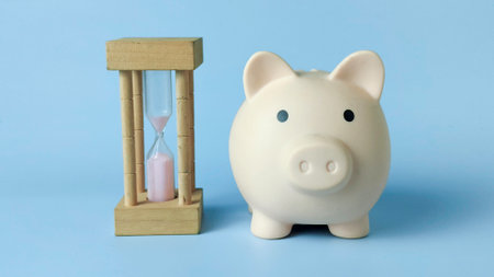 Piggy Bank and Sand Hourglass on Blue Background Representing Financial Planning, Savings, and Time Managementの写真素材