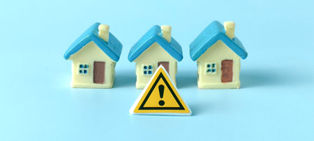 Real Estate Market Risk and Housing Crisis Concept: Three Miniature Houses and a Central Warning Signの写真素材