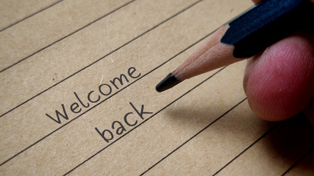 Welcome Back Words Written on Lined Vintage Paper with Hand Holding Pencil Greeting Conceptの写真素材