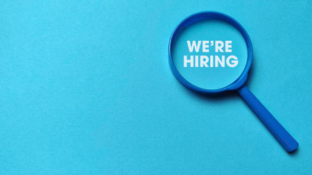 "We're Hiring" message magnified by a blue magnifying glass on matching background for job search and recruitment.の写真素材