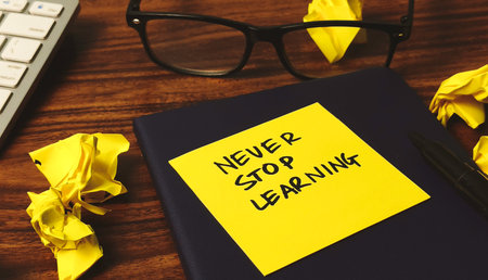 Lifelong Learning Motivation: 'Never Stop Learning' Reminder on Desk with Crumpled Paperの写真素材