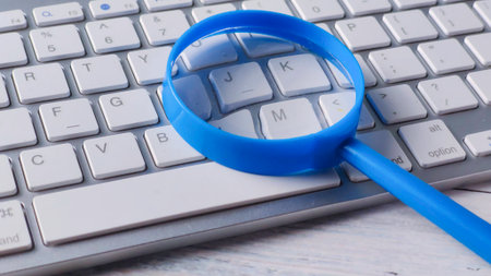 Bright Blue Magnifying Glass Resting on a Modern Wireless Keyboard for Online Search and Digital Investigationの写真素材