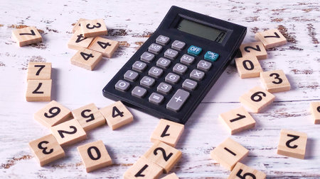 Financial Calculation Chaos: Calculator Surrounded by Scattered Wooden Number Tilesの写真素材