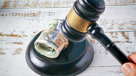 Cost of Justice: Rolled US Dollars Underneath Judge's Gavel on Rustic Surfaceの写真素材