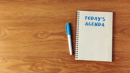Today's Agenda written on a spiral notebook with a blue marker on a wooden desk for planning and business concepts.の写真素材