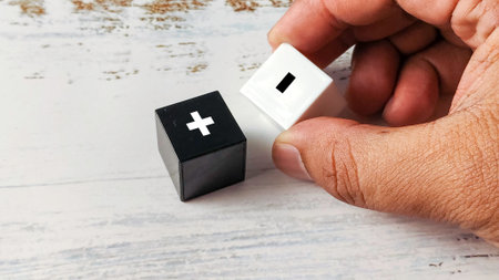 Hand Holding Black and White Cubes with Plus and Minus Symbols, Representing Comparison, Pros, Cons, and Decision Makingの写真素材