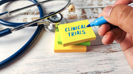 Hand Writing "Clinical Trials" on a Stack of Sticky Notes Next to a Stethoscope, Illustrating Medical Research and Drug Developmentの写真素材