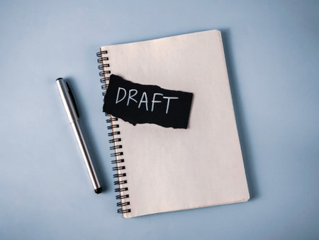 Drafting a Document Concept: Notebook, Silver Pen, and Black Paper with White 'Draft' Text for Writing and Revisionの写真素材