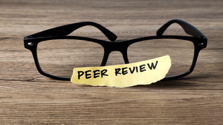 Peer Review concept with a handwritten note placed on reading glasses on a wooden desk, symbolizing academic research and quality assurance.の写真素材