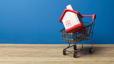 Red and white toy house inside a miniature shopping cart for real estate purchase and home buying.の写真素材