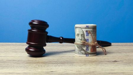 Wooden judge gavel next to a roll of hundred dollar bills representing legal fees and litigation...
