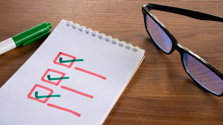 A hand drawn checklist with green check marks in red boxes on a white notepad with a marker and glasses nearby.