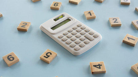 High angle perspective of a white desk calculator surrounded by scattered wooden number tiles, concept of business analysis, financial audit, and math education.