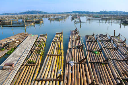 bamboo raft leaning against a lake among traditional fish cages in indonesia, asiaの写真素材