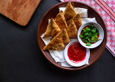 Samosa, samsa or somsa are triangular fried pastries or pastri served with tomato sauce and leek slice, on  tableの写真素材