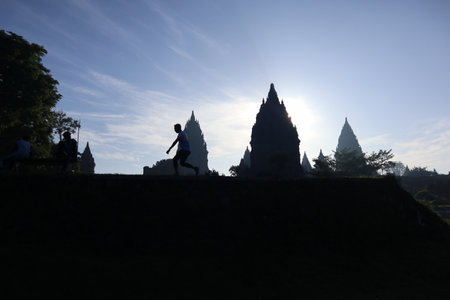 silhouette of a man running, jogging at Prambanan temple in the morning, with sky blue backgroundの写真素材
